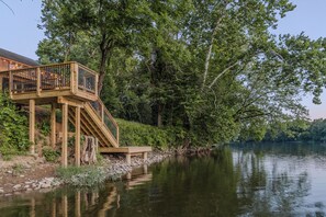 Eine Holzterrasse mit Treppe zu einem Balkon mit Blick auf einen Fluss, umgeben von Bäumen.