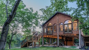 Une cabane en bois dotée d’une terrasse, de grandes fenêtres et d’un escalier menant à un balcon.