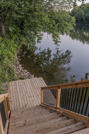 Eine Holzterrasse führt zu einem ruhigen See, umgeben von dichtem Grün.