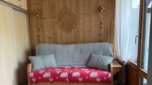 Een gezellige kamer met een houten wand, een bank met geruit kussens, en een raam met gordijnen.