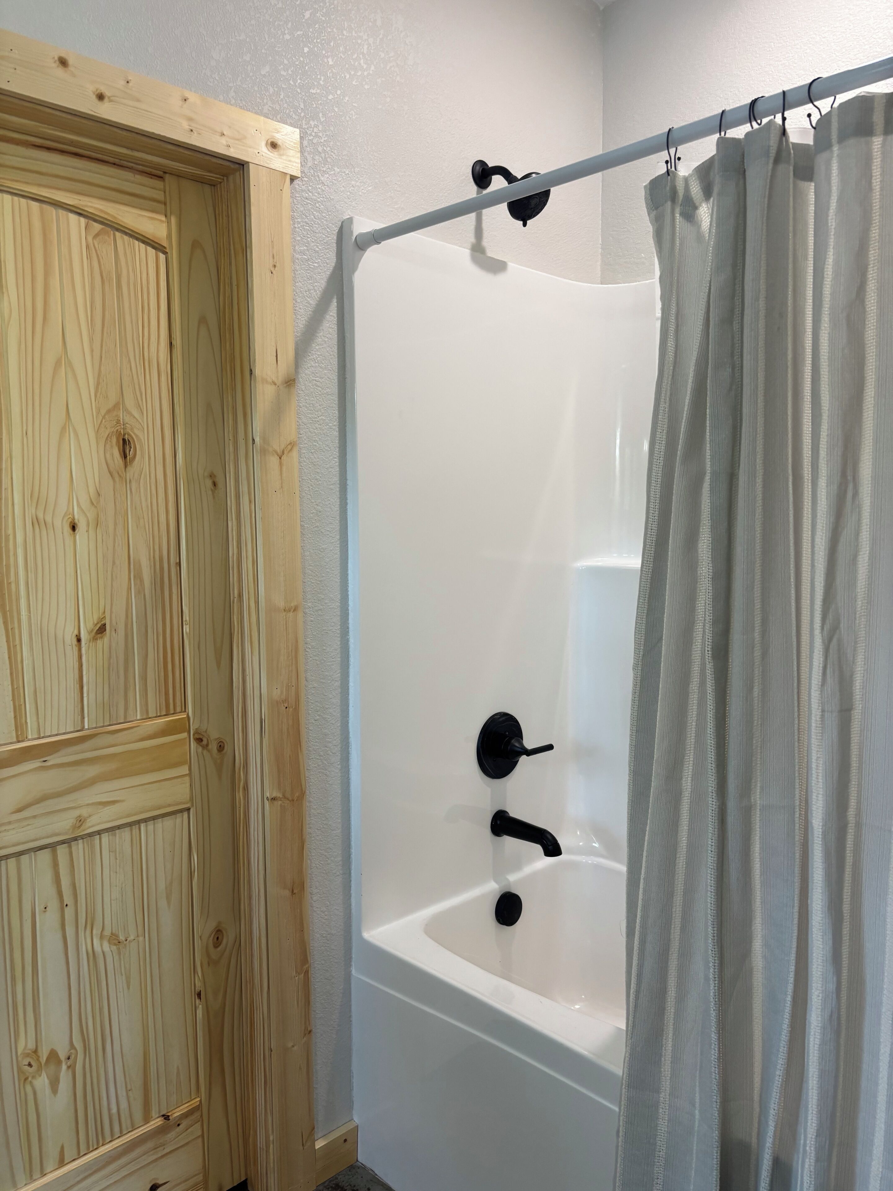 Une salle de bain avec une porte en bois, une baignoire et un rideau de douche.