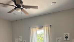 Un dormitorio con dos camas, un ventilador de techo, una ventana con cortinas y decoración en la pared.