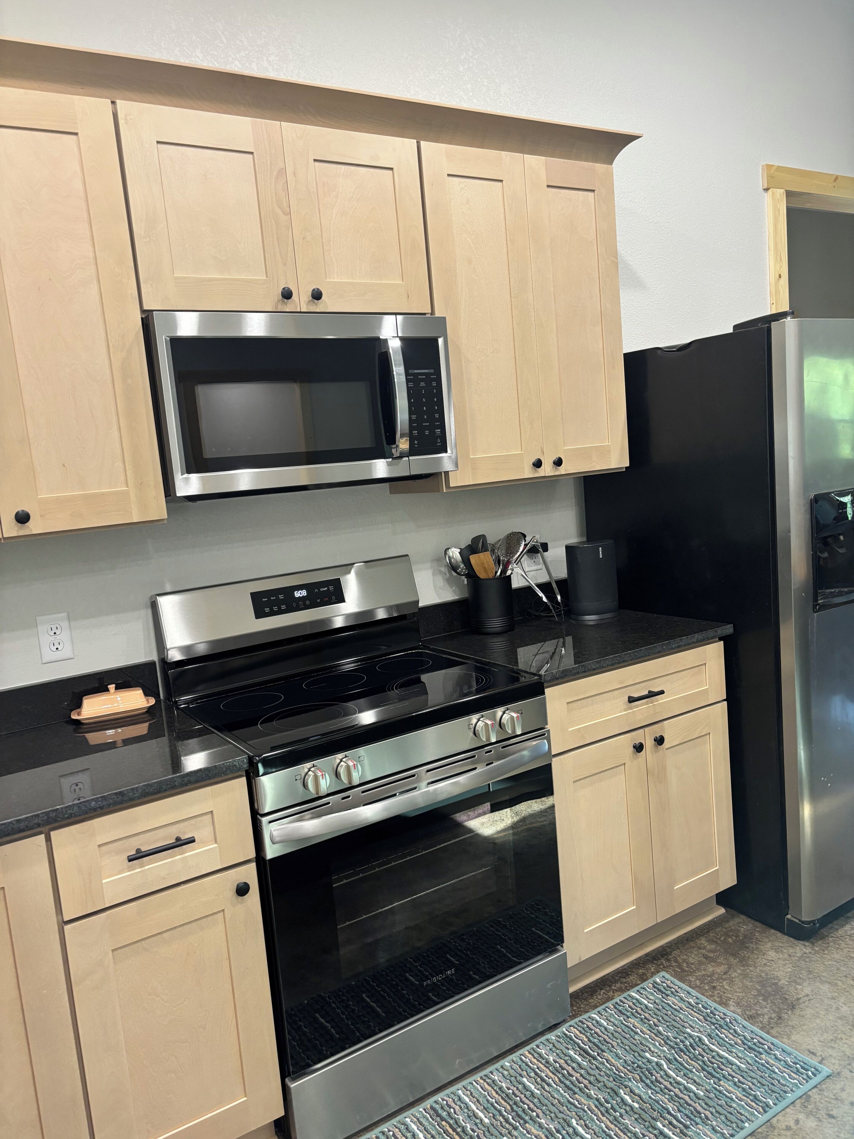 A kitchen with light wooden cabinets, a stainless steel microwave, a black stove, and a black refrigerator.