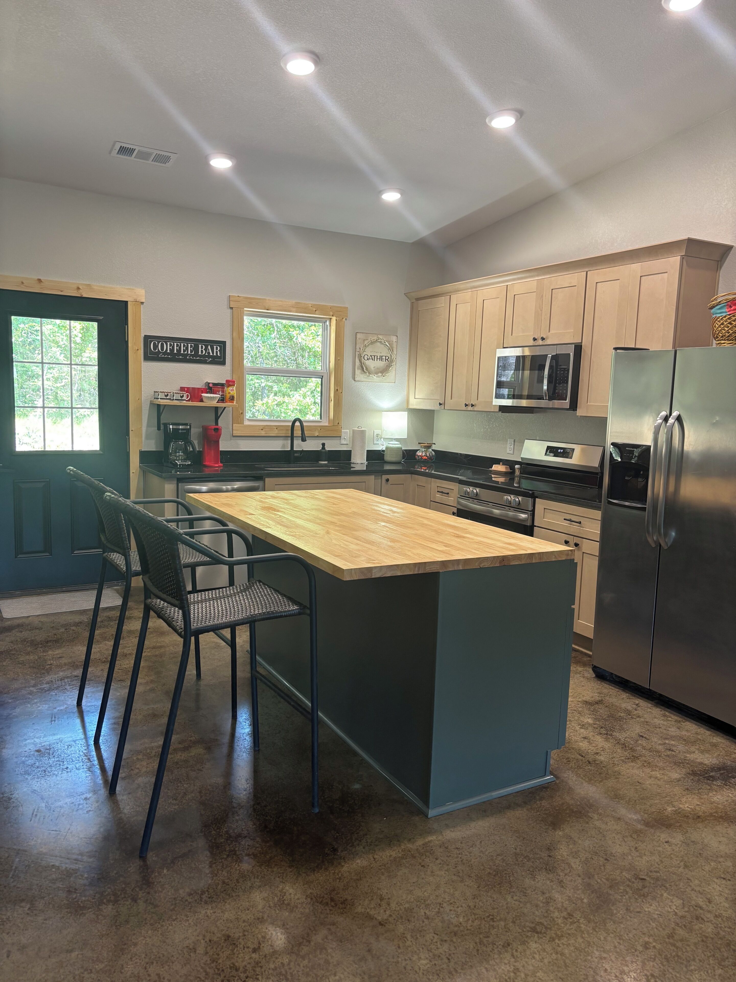 A modern kitchen with a central island, black bar stools, a coffee bar, and a microwave.