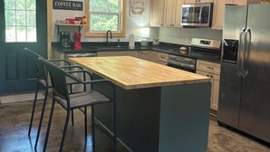 Una cocina moderna con una isla central, taburetes negros tipo bar, una barra para café y un microondas.