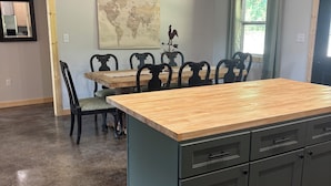 Cocina con isla de madera, armarios oscuros y un comedor con sillas y mesa.