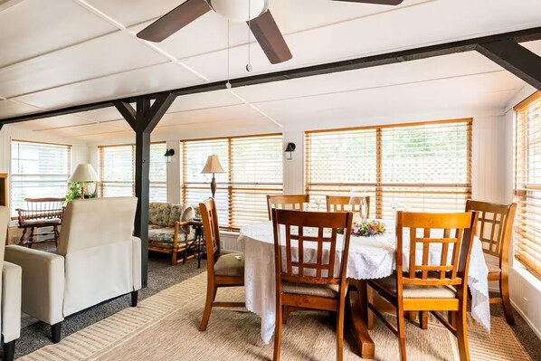 A dining area with a table set for four, surrounded by wooden chairs, a ceiling fan, and large windows with blinds. - 3-bedroom, 2-bath house in beautiful downtown Bastrop.  Great yard and scenery. (Bastrop)