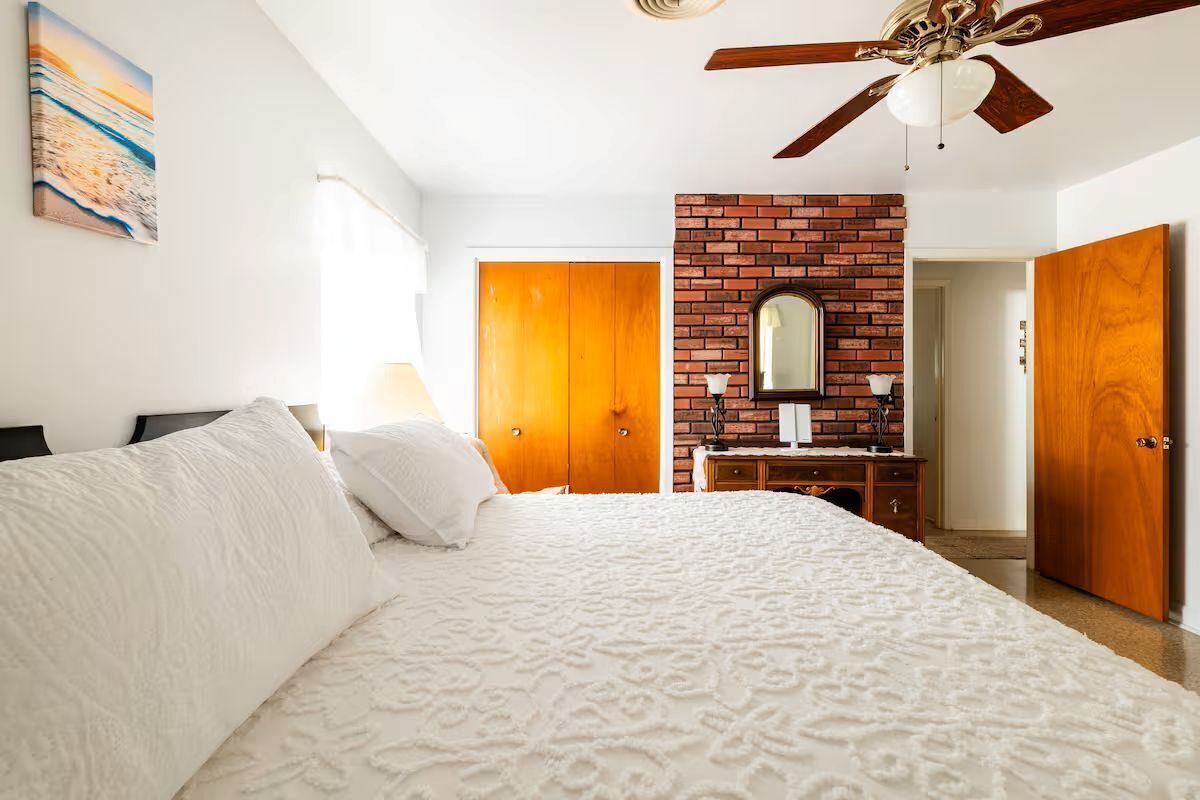 Ein Schlafzimmer mit einem großen Bett, einer Ziegelfassade, einem Deckenventilator und Holztüren.