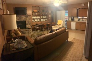 A living room with a sofa, a coffee table, and a fireplace. There is a kitchen area with cabinets and a refrigerator. - 3-bedroom, 2-bath house in beautiful downtown Bastrop.  Great yard and scenery. (Bastrop)