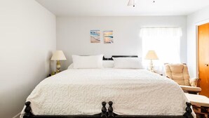 Un dormitorio con cama, dos lámparas de noche, una silla y un ventilador de techo.