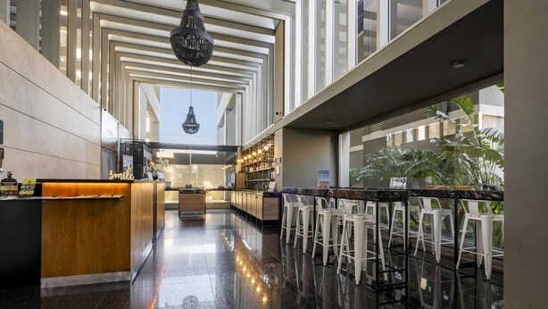 Zona de bar moderna amb un sòl polit, una taquilla de fusta i tamborets blancs.