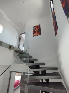 Eine moderne Treppe mit Glastrennwand, ein Gemälde an der Wand und eine Tür zu einem anderen Raum.