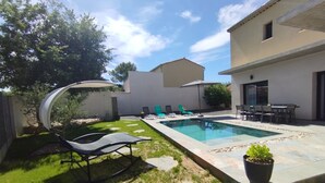 Um quintal com piscina, espreguiçadeiras, mesa de jantar e um vaso de planta.