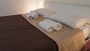 Ein Bett mit einer braunen Bettdecke mit Fischgrätmuster, zwei gerollte weiße Handtücher und ein weißes Kopfkissen.