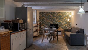 Eine kompakte Küche mit Kühlschrank, Mikrowelle und Kaffeemaschine, ein Essbereich mit Tisch und Stühlen sowie ein graues Sofa.