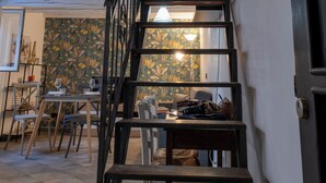 Eine Treppe führt zu einer zweiten Etage mit Geländer, einem Essbereich mit Tischen und Stühlen sowie einer Wand mit Muster.