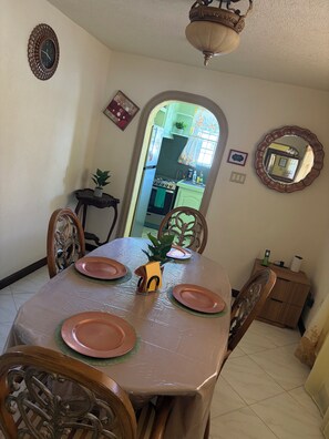 A dining area with a table set for four, chairs, a decorative mirror, and a view into a kitchen. - Christoph Escape Barbados (Bridgetown)