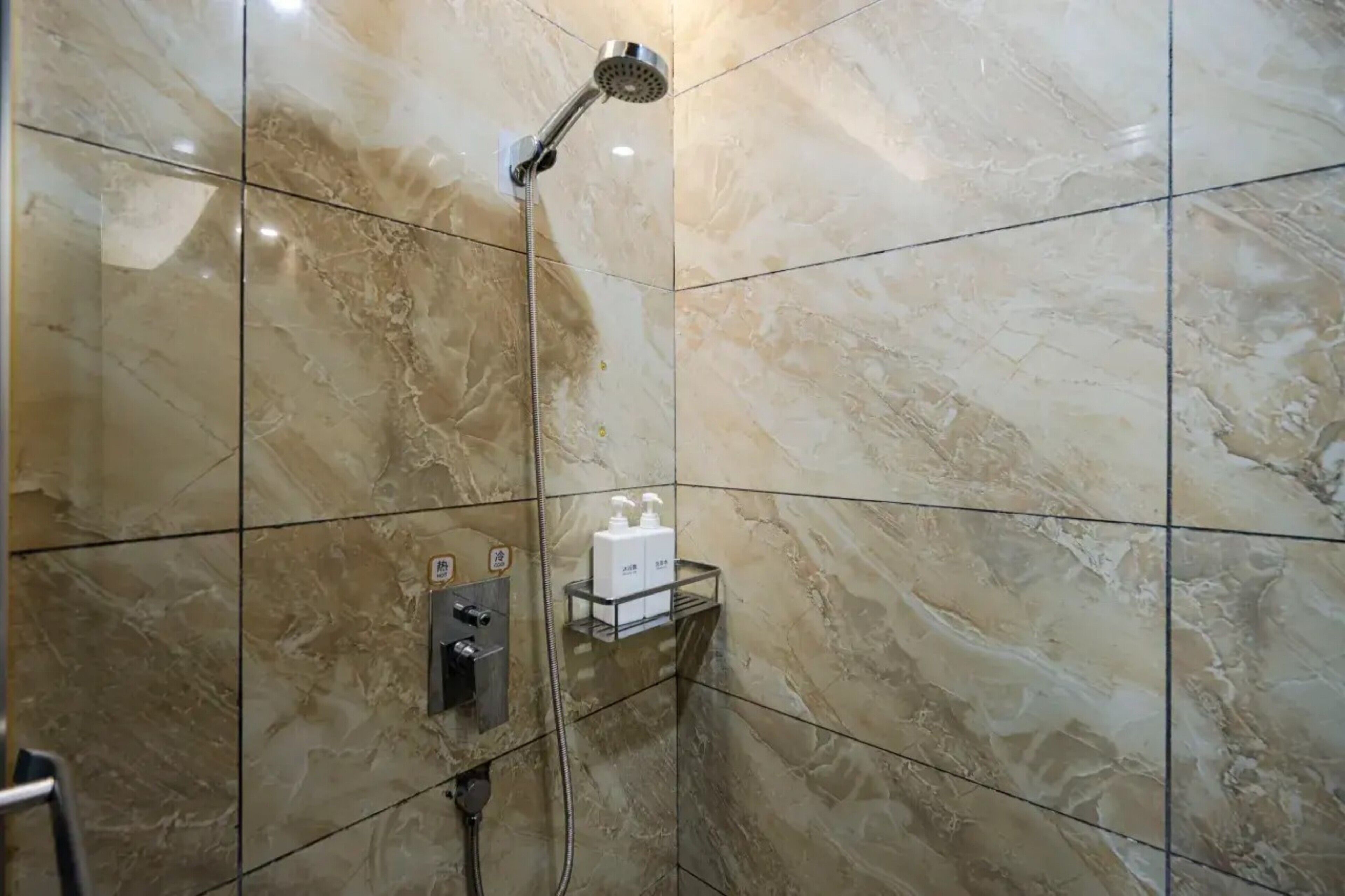 A bathroom with a shower, marble tiles, a towel rack, and a soap dispenser.
