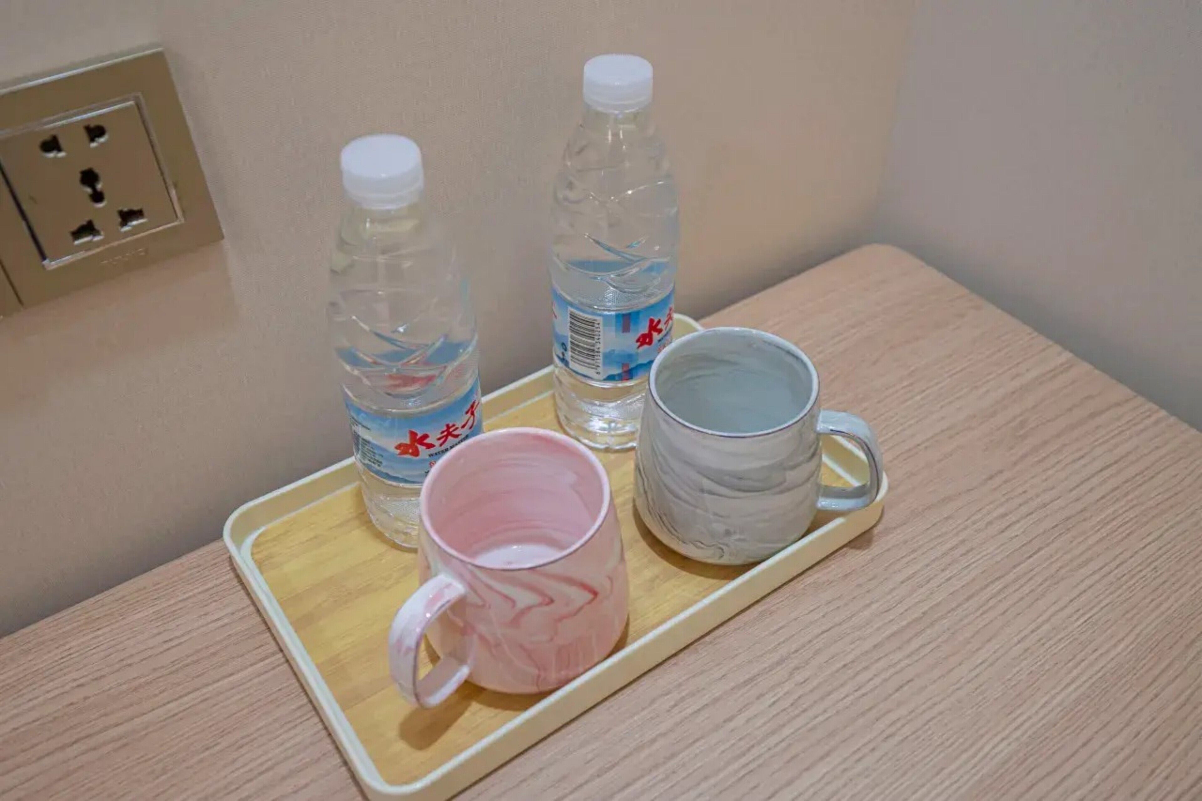 Una bandeja con dos botellas de agua, una taza rosa y una taza gris sobre una mesa de madera.