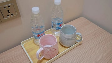Una bandeja con dos botellas de agua, una taza rosa y una taza gris sobre una mesa de madera.
