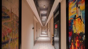 A hotel corridor with a geometric patterned floor, a ceiling with a hexagonal design, and a large abstract painting on the right wall. - Pebble Motel Fuzhou Fuxin Middle Road (Fuzhou)