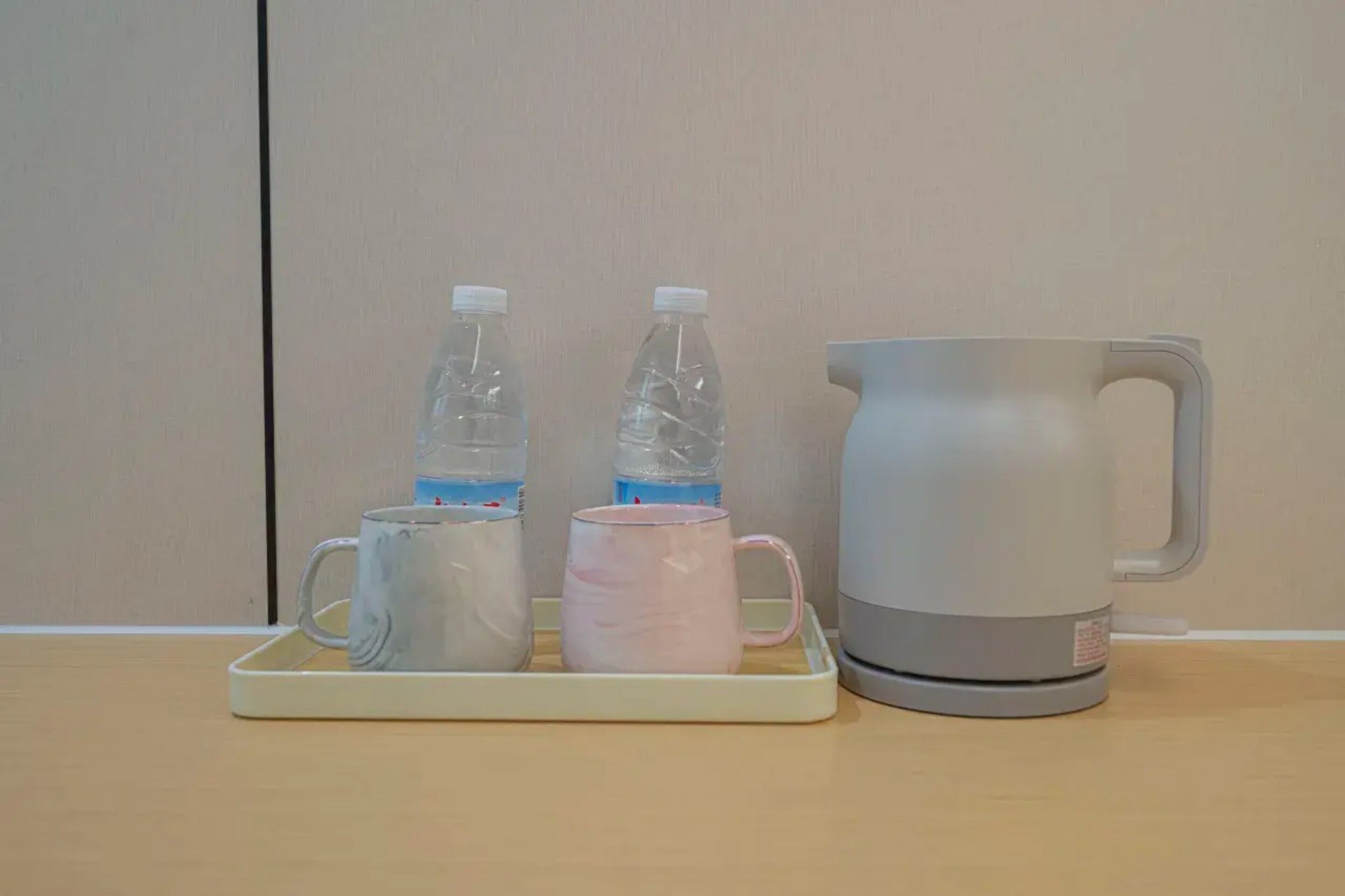 A tray with two water bottles, a pink mug, and a gray pitcher on a wooden surface.