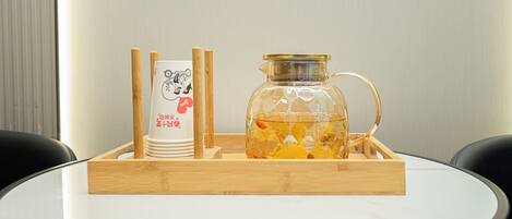 A table with a glass decanter and a stack of white cups with a logo, placed on a wooden tray.