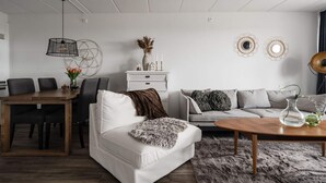 Ein modernes Wohnzimmer mit einem weißen Sofa, einem Holztisch, einem Esstisch mit Stühlen und Wanddekoration.