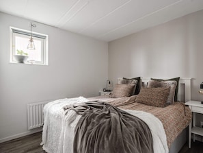 Quarto com cama, mesas de cabeceira, radiador, janela com planta e luminária pendente.