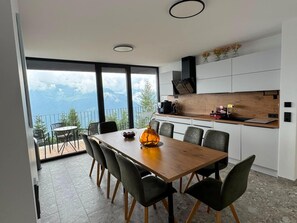 Une cuisine moderne avec un plan de travail en bois, une table à manger avec des chaises et une vue sur les montagnes grâce à de grandes fenêtres.