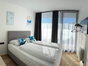 Una habitación de hotel moderna con una cama curvada, ropa de cama blanca y un ventanal con cortinas translúcidas.