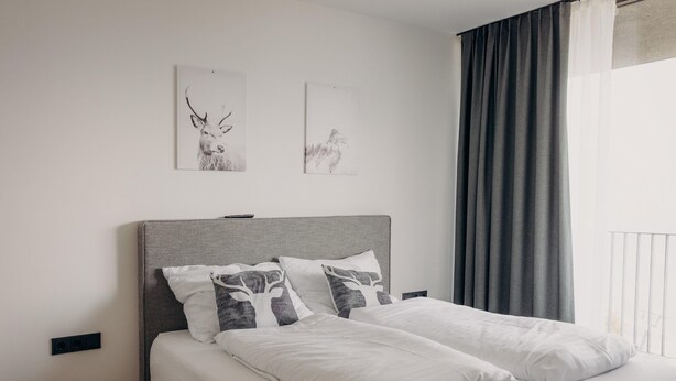 A neatly made bed with white linens and two pillows, a grey headboard, and two wall-mounted pictures of animals. - Panorama Apartment Monte Central (Neukirchen am Grossvenediger)