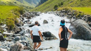 Two people standing on rocks by a flowing river with mountains in the background. - Panorama Apartment Monte Central (Neukirchen am Grossvenediger)