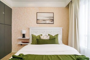 Habitación de hotel ordenada con cama, mesita de noche con lámpara, un cuadro en la pared y vistas al exterior.