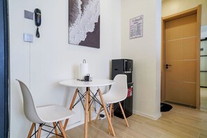 Una habitación pequeña con una mesa blanca y dos sillas, un teléfono en la pared, un dispensador de agua y una puerta con marco de madera.