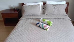 A neatly made bed with a quilted white duvet, two pillows, and two rolled towels on the bed. - Dorado Eagle Beach Hotel (Eagle Beach)