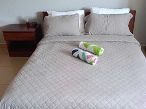 Una cama bien hecha con un edredón blanco acolchado, dos almohadas y dos toallas enrolladas sobre la cama.