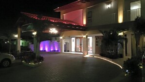 A hotel entrance with a red awning, a paved driveway, and a landscaped area with plants. - Dorado Eagle Beach Hotel (Eagle Beach)