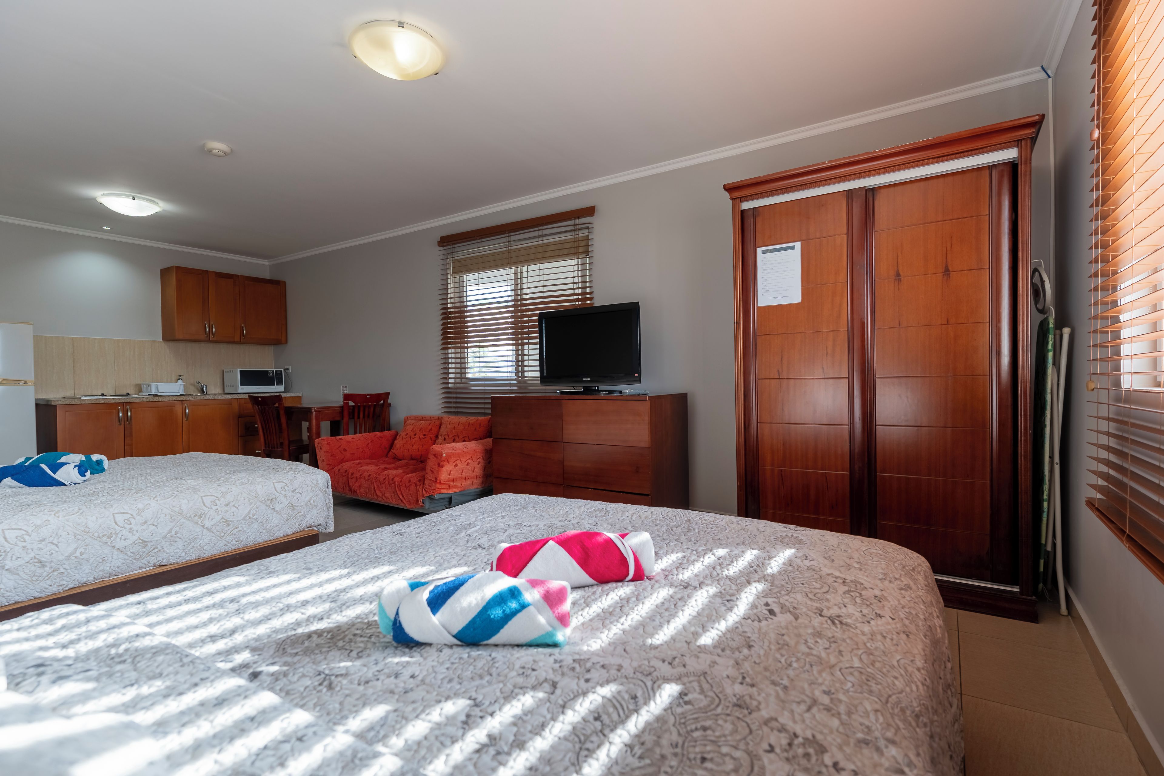 Ein Hotelzimmer mit zwei Betten, einem Fernseher, einem Schreibtisch mit Computer und einem Kleiderschrank.