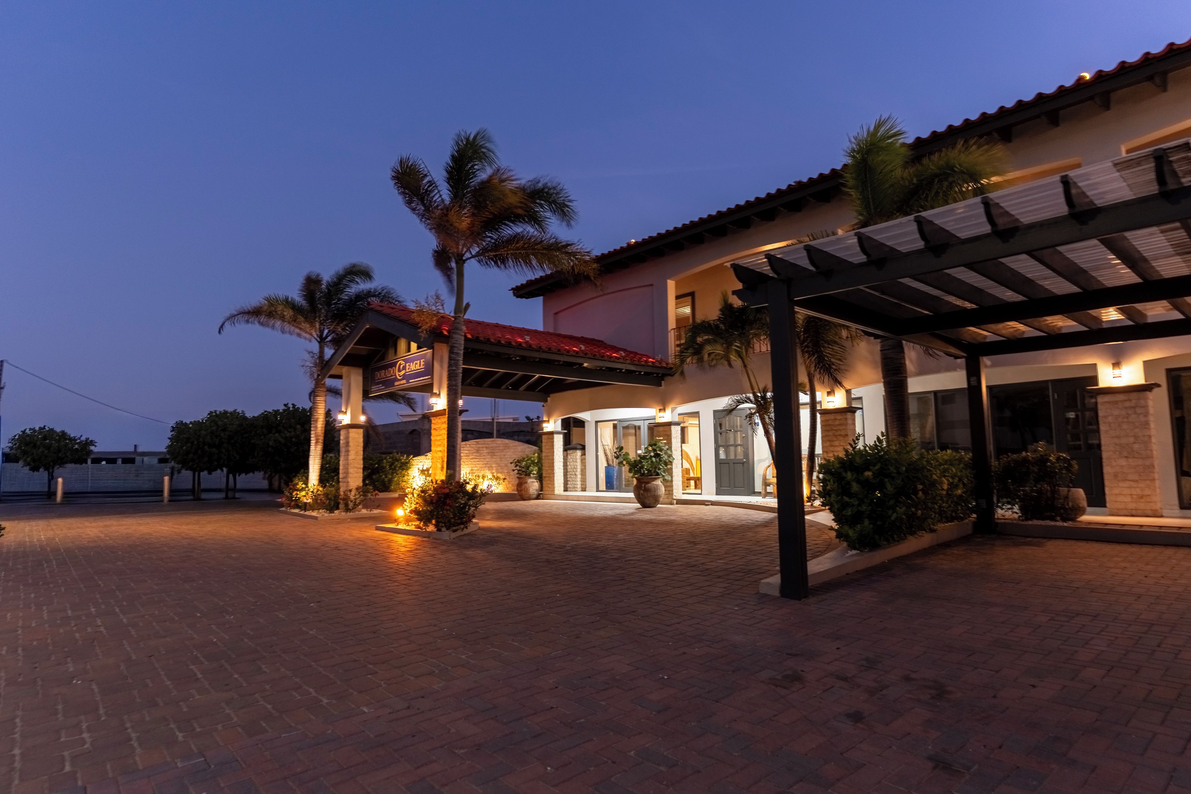 Entrada de hotel con un patio cubierto, palmeras y un camino de ladrillo.