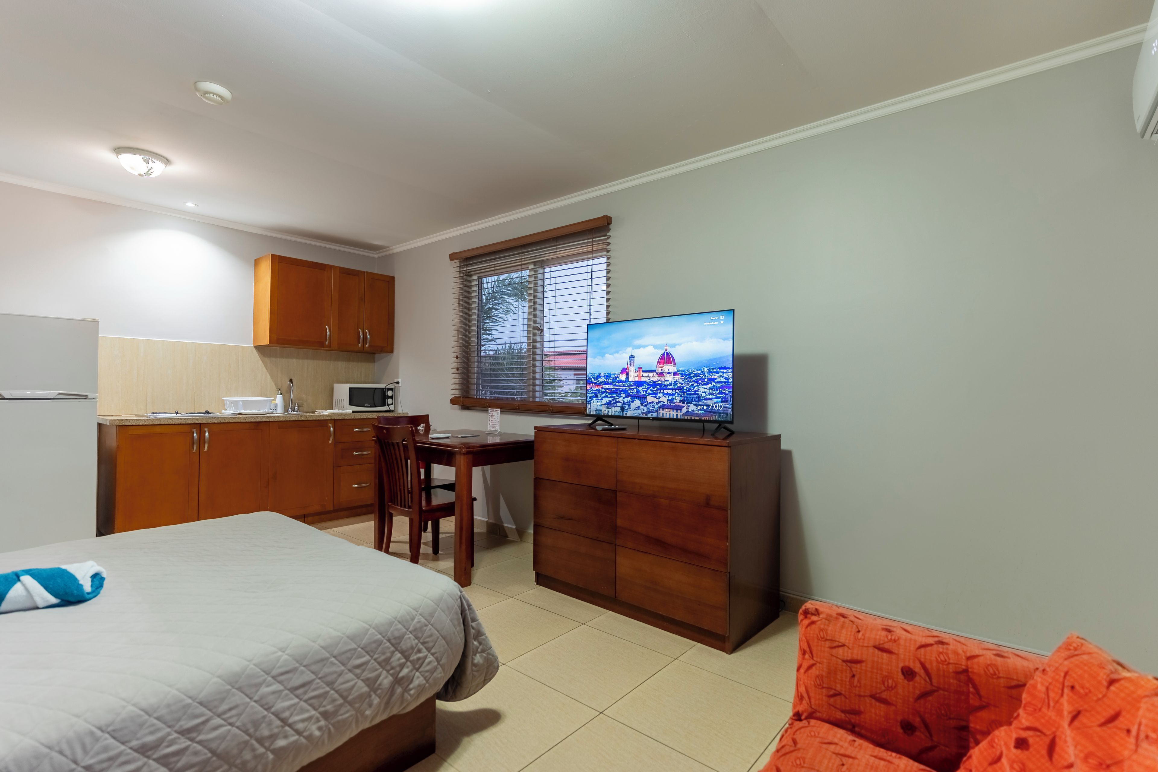 A compact room with a bed, a desk, a television, and a kitchenette.