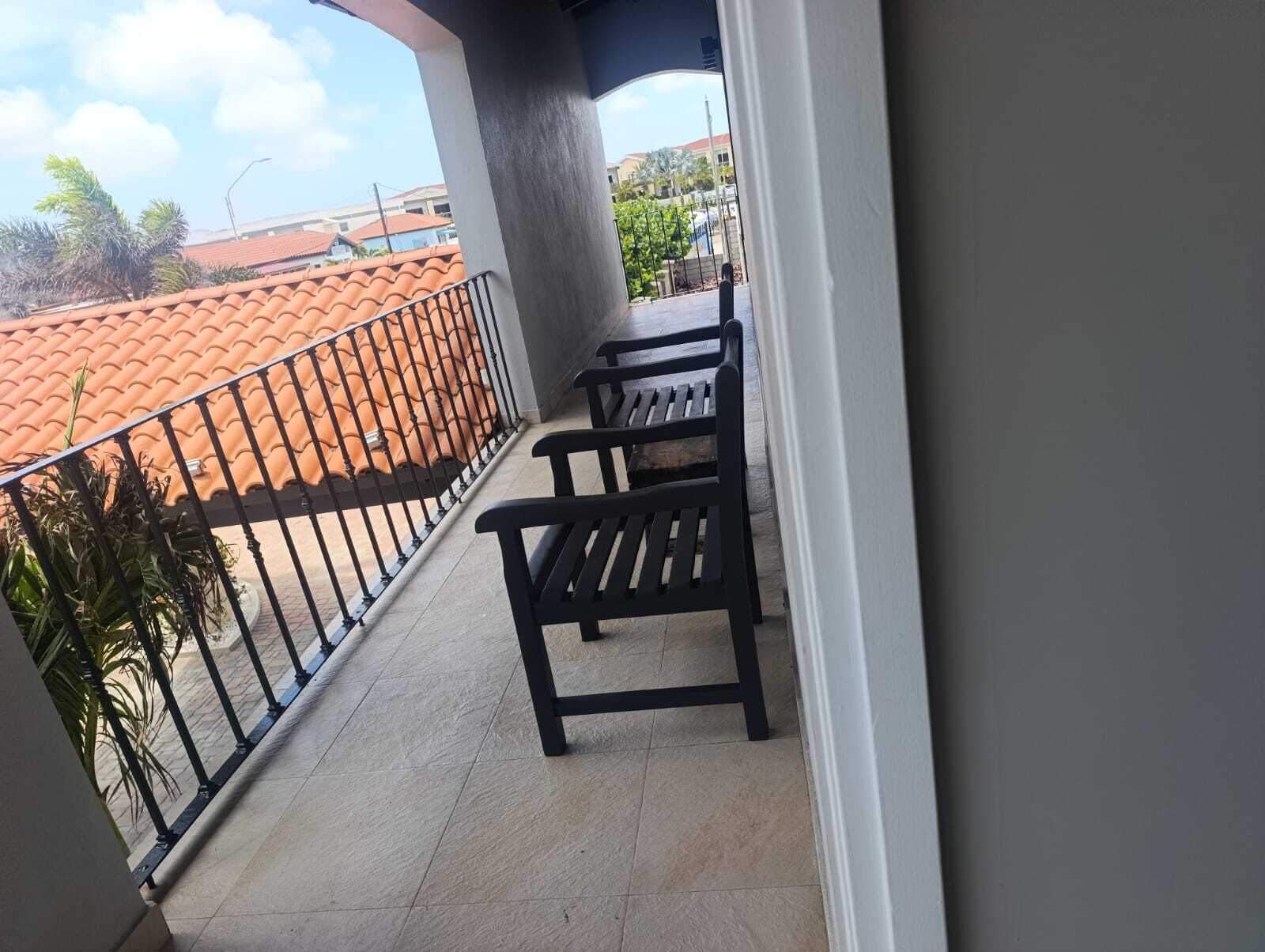 Ein Balkon mit gefliestem Boden, einem Metallgeländer und zwei schwarzen Stühlen.