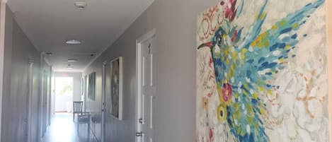 Un pasillo con un cuadro abstracto grande en la pared, una puerta a la derecha y una silla al fondo.