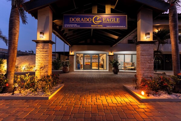 The Dorado Eagle Beach Hotel entrance with a brick pathway leading to the doors, palm trees, and a sign above the entrance.