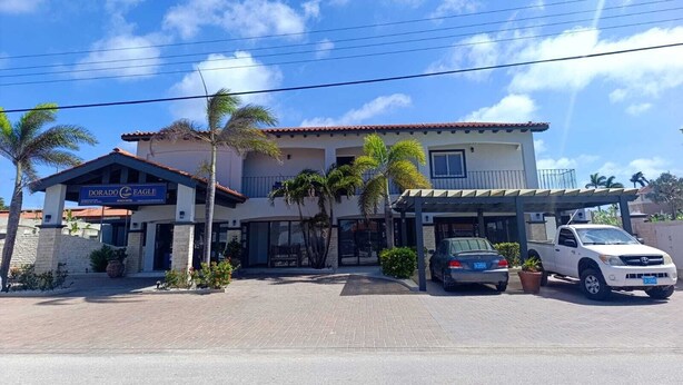 A hotel with a signboard, a covered parking area, and a white pickup truck parked in front. - Dorado Eagle Beach Hotel (Eagle Beach)