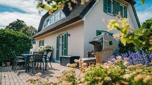 Une maison avec un toit de chaume, des volets verts et un jardin fleuri.