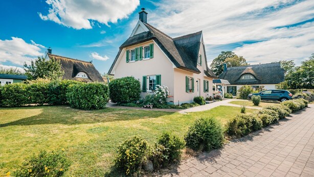 Une maison avec un toit de chaume, une pelouse bien entretenue et une allée pavée.