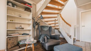 Un salon avec une bibliothèque, un fauteuil, une petite table et un escalier.