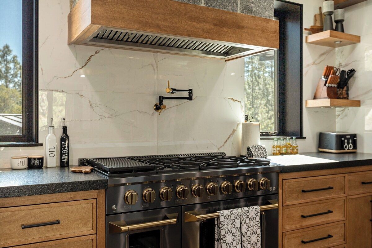 A kitchen with a gas stove, wooden cabinets, a marble backsplash, and a window with a view.