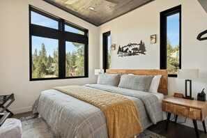 Quarto com uma cama grande, duas janelas, cabeceira de madeira, mesa de cabeceira e luminária na parede.